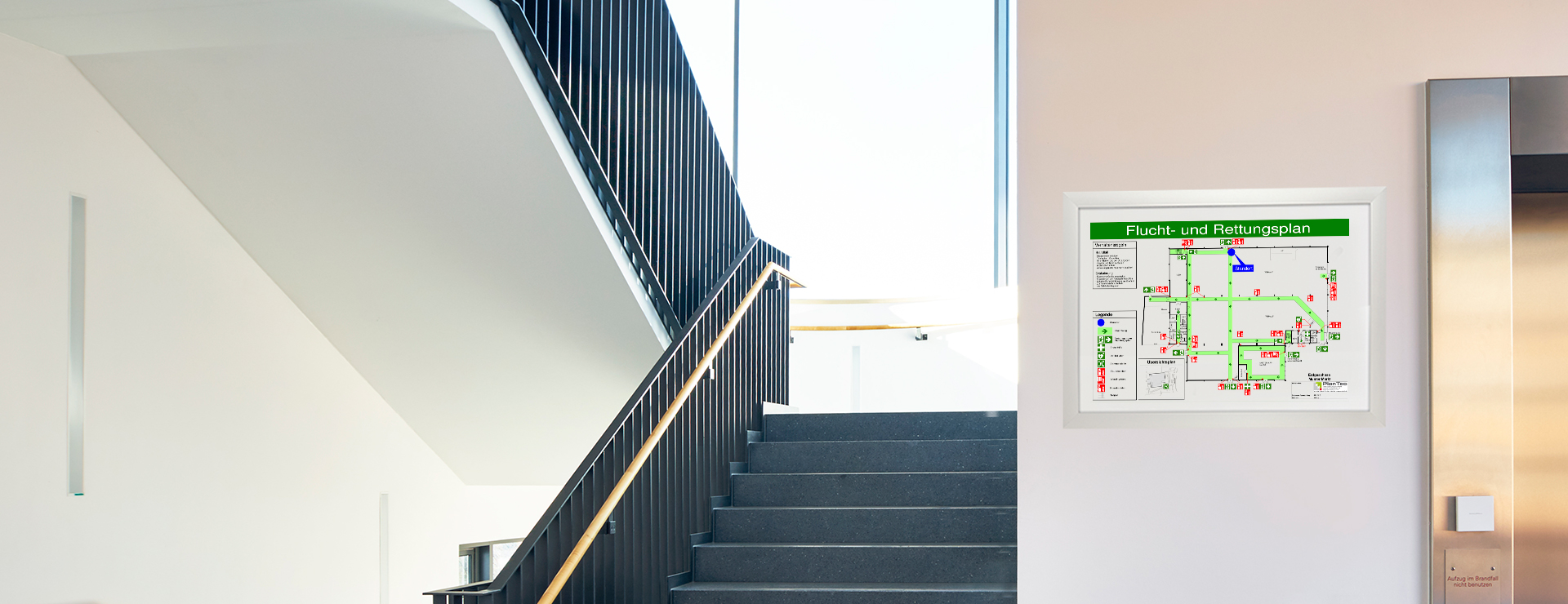 Treppenhaus in einem modernen Gebäude, Neben dem Aufzug hängt ein Flucht- und Rettungsplan